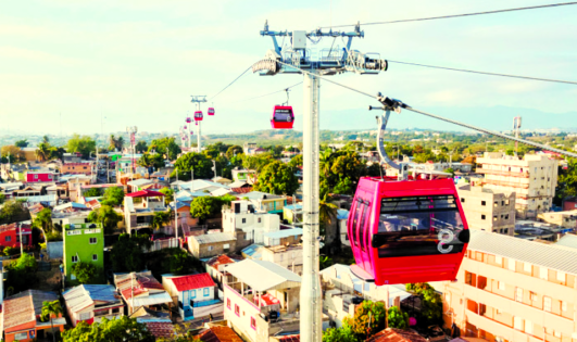 Teleférico de über Santiago de los Caballeros Eine Seilbahn mit roten und pinken Gondeln über einer Stadtlandschaft.