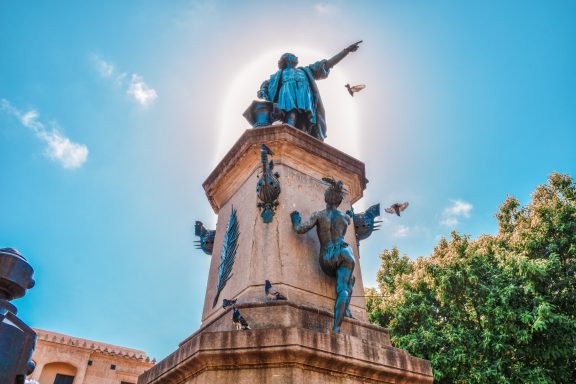 KOLUMBUS war auch schon hier Sonnenumrahmter Standpunkt einer Statue mit einer Figur, die nach oben zeigt.
